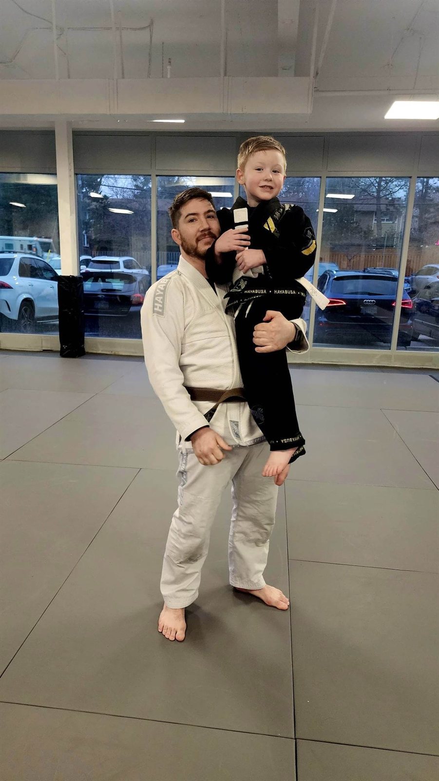 A coach lifting up a smiling young student in his gi